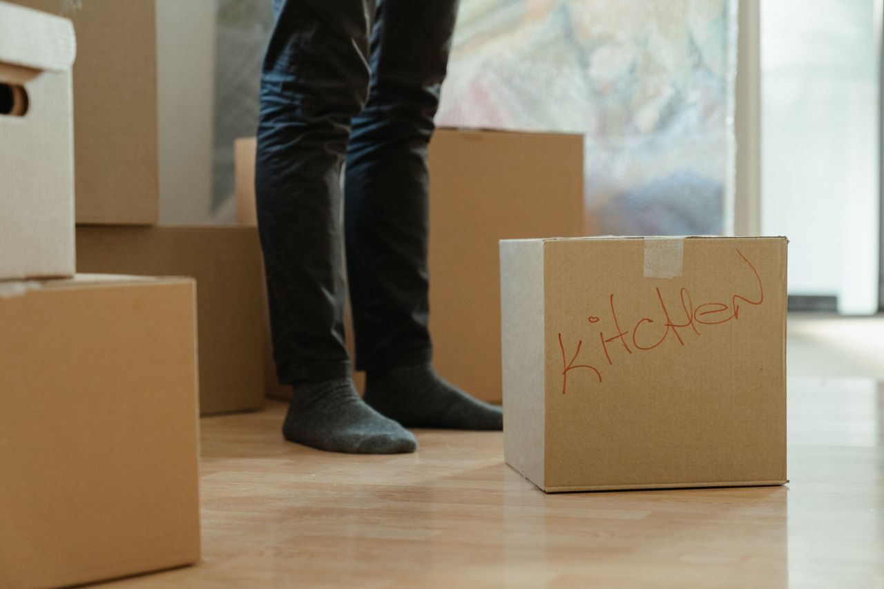 Une personne debout dans une pièce, entourée de cartons de déménagement étiquetés pour la cuisine.